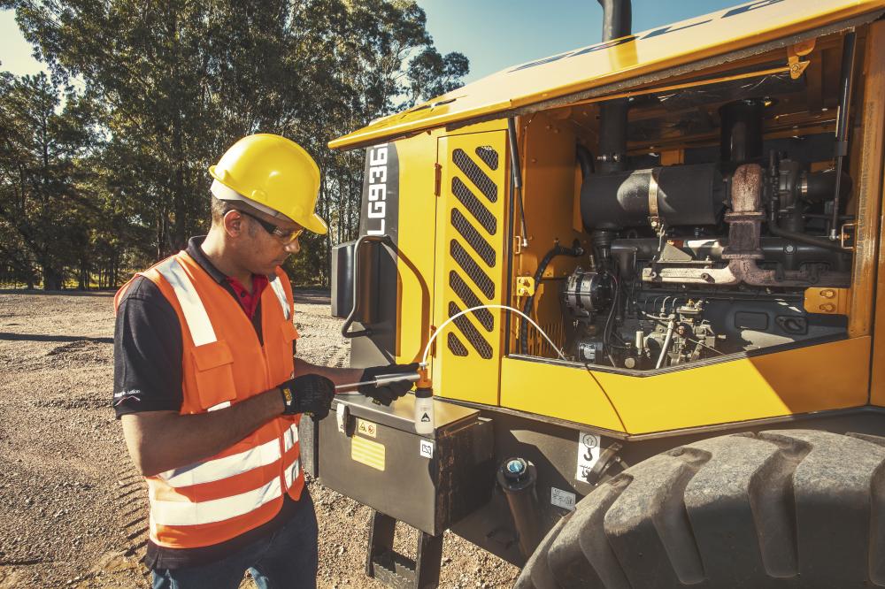 Um homem usando colete laranja e capacete amarelo realizando a análise do óleo no modelo LG 936